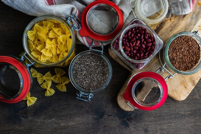 Top view of ingredients in glass containers with pasta, seeds and beans on wooden background with copy space