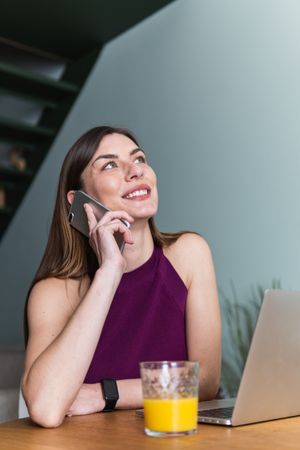 Smiling woman using smartphone and sitting at table with laptop