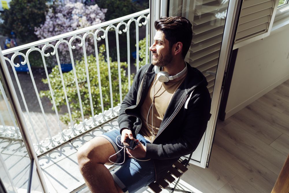 Young happy man holding smartphone on balcony