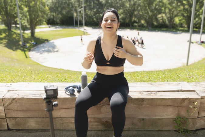 A young woman laughs happy while records herself on video, to explain to her followers, how to perform an exercise and sport workout