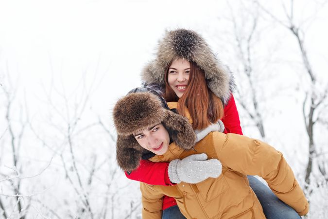 Smiling teenage girl on back on boyfriend in snowy forest