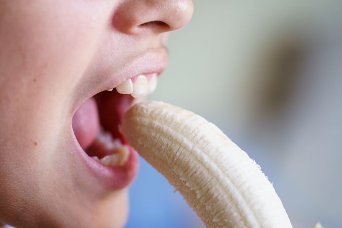 Teenage girl with mouth open eating fresh peeled banana