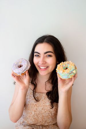 Playful woman making glasses of donuts while standing by white wall