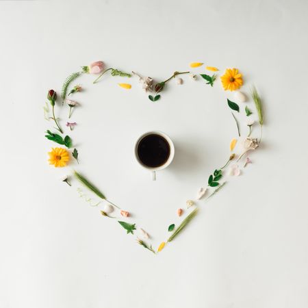 Heart shape made of yellow flowers and leaves with coffee