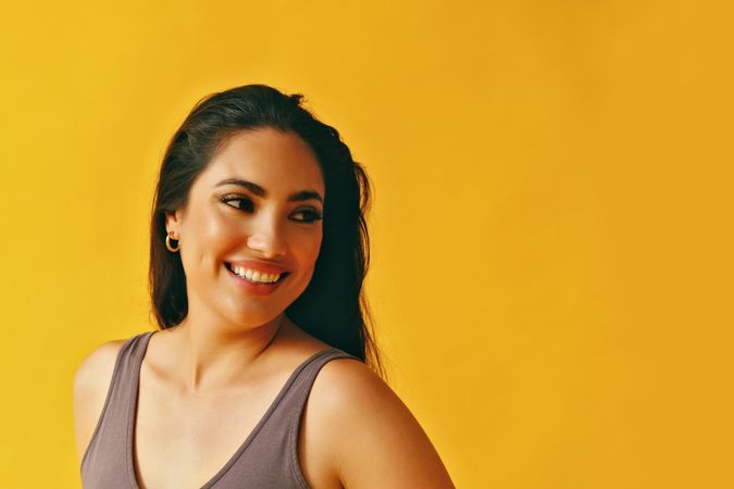 Headshot of Hispanic woman with head looking to side on yellow background
