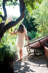 Little girl with curly, light hair walking on a path in her garden away from the camera