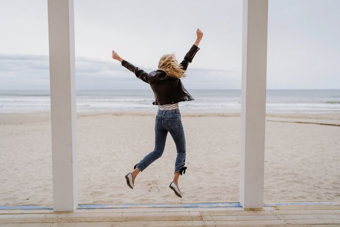 Joyful woman jumping raising hands up on wooden beach pier