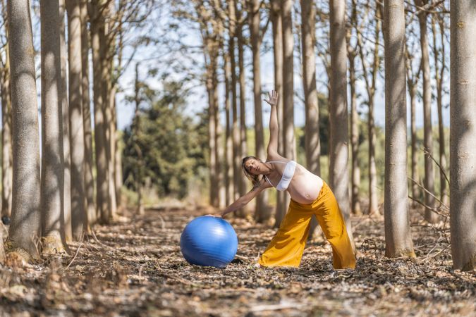 Adult pregnant woman training with pilates ball in park during sunny day