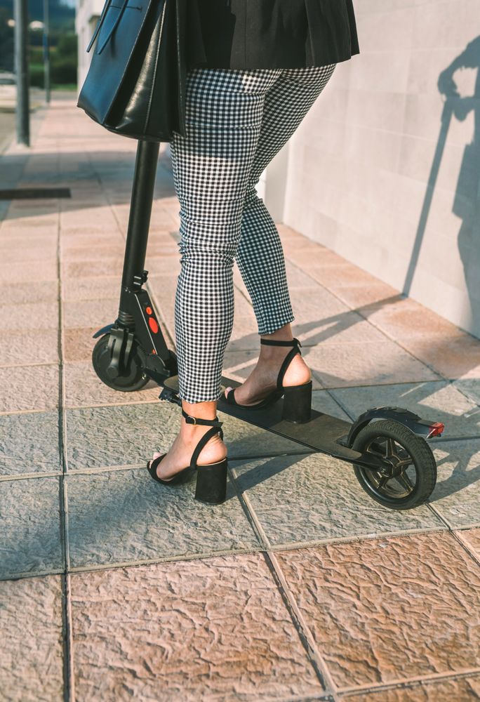 Unrecognizable businesswoman legs with e-scooter outdoors
