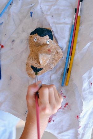 Unrecognizable child painting stone with gouache