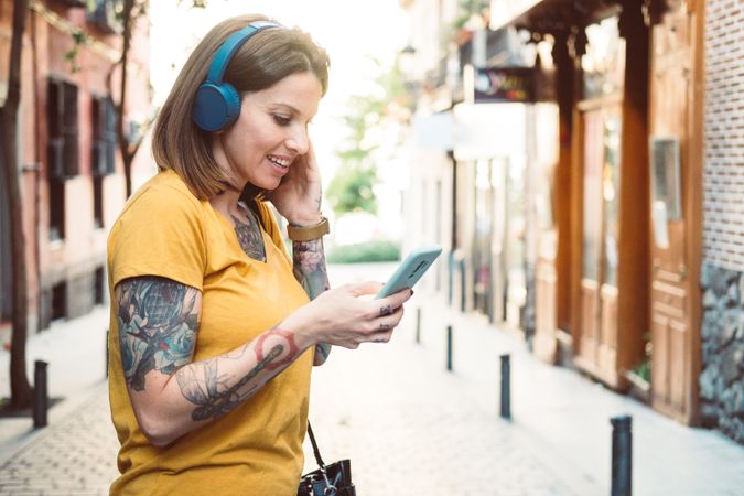 Inspired woman in headphones listening to music on smartphone on street