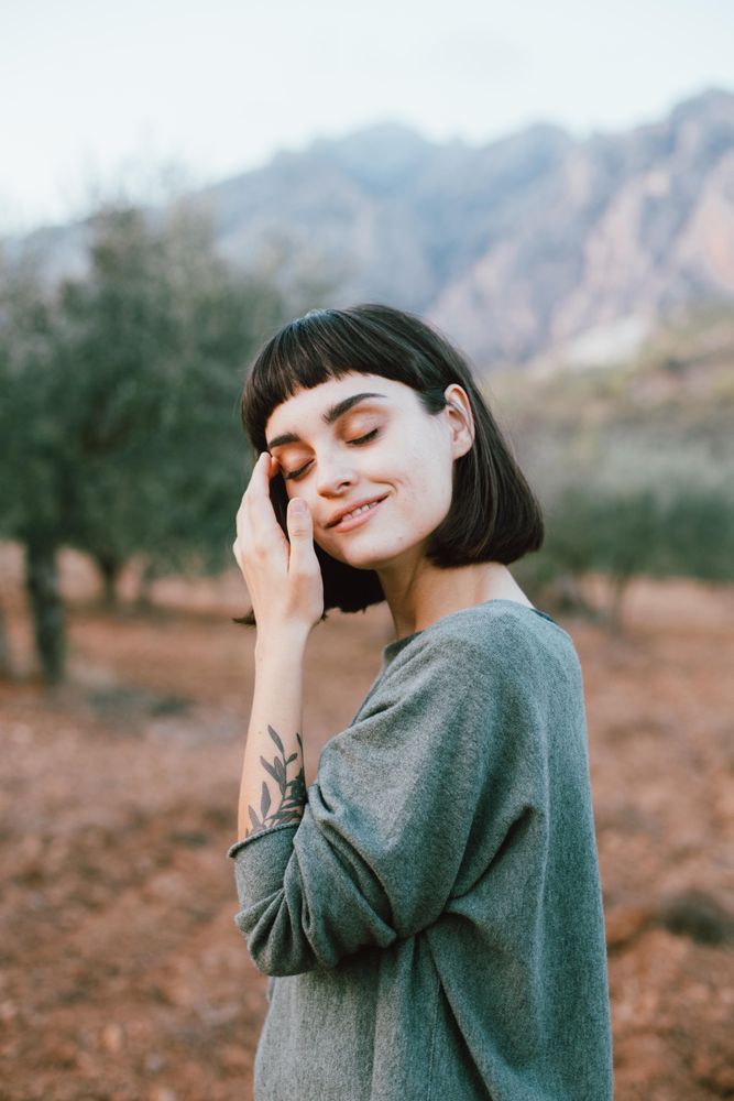 Woman with eyes closed in beautiful park with hills and olive trees