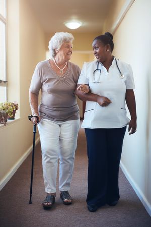 Mature woman with walking stick being helped by female nurse at home