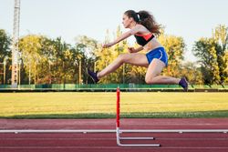 An athletic woman jumping hurdles on an athletics track.