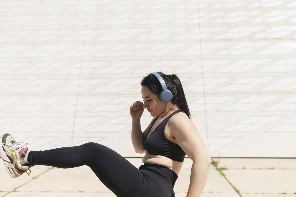 A woman kicks her leg in the air while listens to music in the sun after exercising