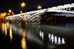 Triana Bridge over Guadalquivir river at sunset with reflections in the water