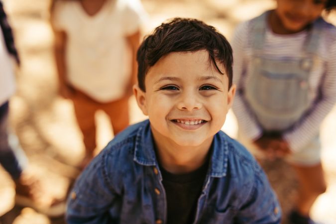 Close up portrait of cute boy smiling at camera with friends at background