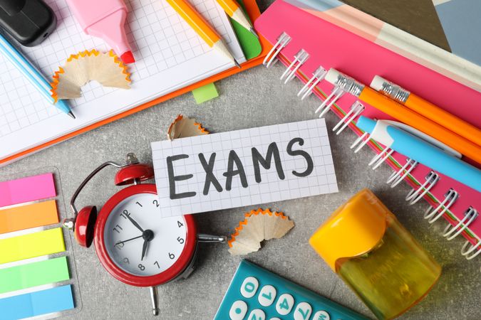 Top view of the word “Exams” surrounded by clock and stationary on desk