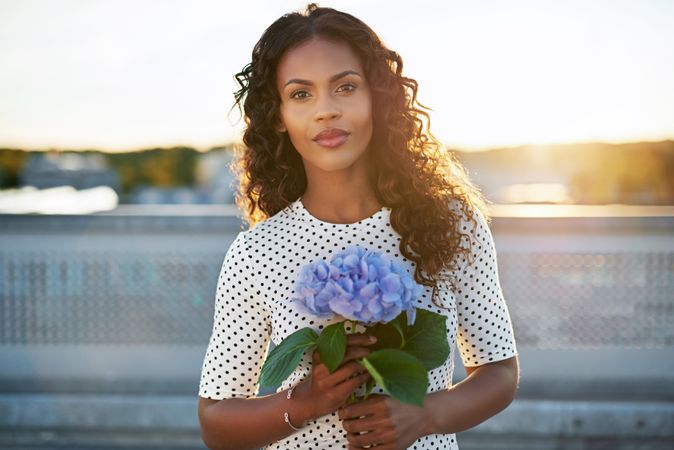 Beautiful Black woman holding a blue flower on a sunny rooftop