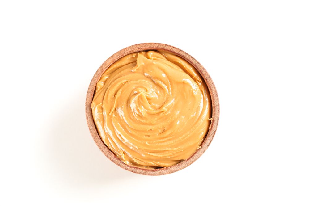 Creamy peanut butter in wooden bowl isolated on light background, top view. A traditional product of American cuisine