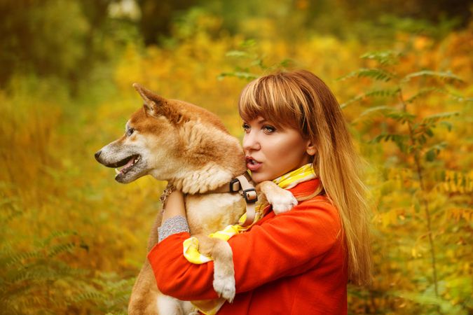 Female in red coat holding her curious shibu dog standing in field
