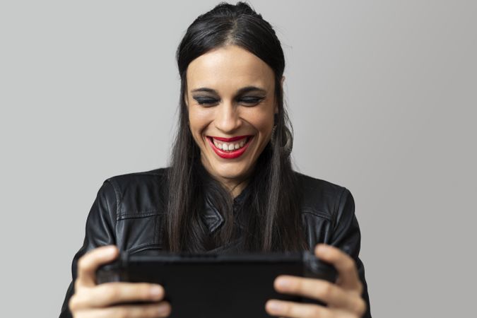 A young woman, with red lipstick, laughs happily as she plays with a handheld video game console she holds in her hands