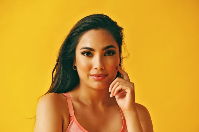 Headshot of curious Hispanic woman standing in front of a yellow background