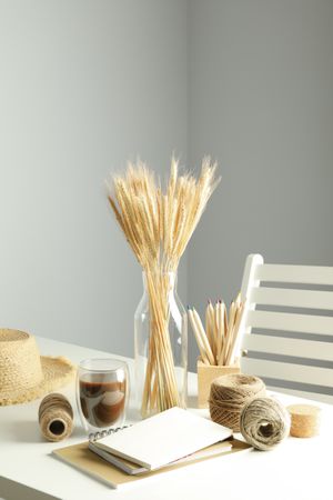 Work table with yarn, notebooks, pencils, dried flowers, with hat and chair, vertical