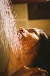 Crop woman catching shower water with mouth