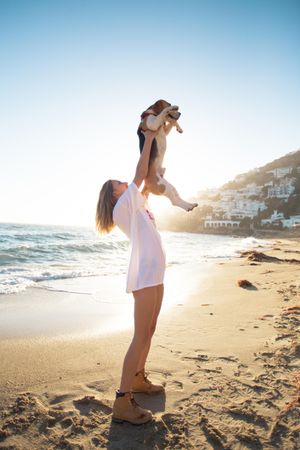 Woman holds up dog on beach