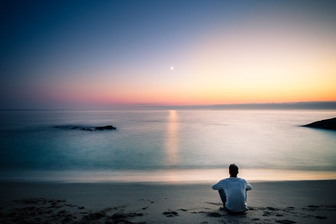 Man sitting on sandy beach during sunset