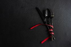 Dark cutlery on dark background tied with bright red ribbon