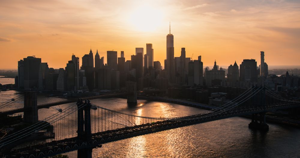 New York City Skyline Aerial Shot from a Helicopter at Sunset. Famous Skyscraper Buildings with Manhattan and Brooklyn Bridges. Busy Diverse Megapolis with Cars, Boats and People Moving Around