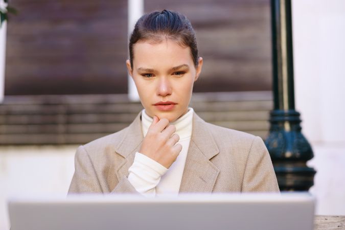 A pensive woman is diligently working on her laptop while seated in a beautiful outdoor setting
