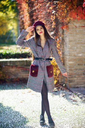 Calm female in warm winter clothes standing outside on sunny day holding her hat