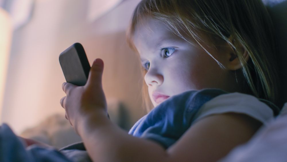 Close-up Shot of a Little Girl Watches Cartoons on a Smartphone in a Bed.