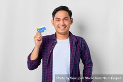 Happy Asian male in grey studio with credit card held up beQ6lb