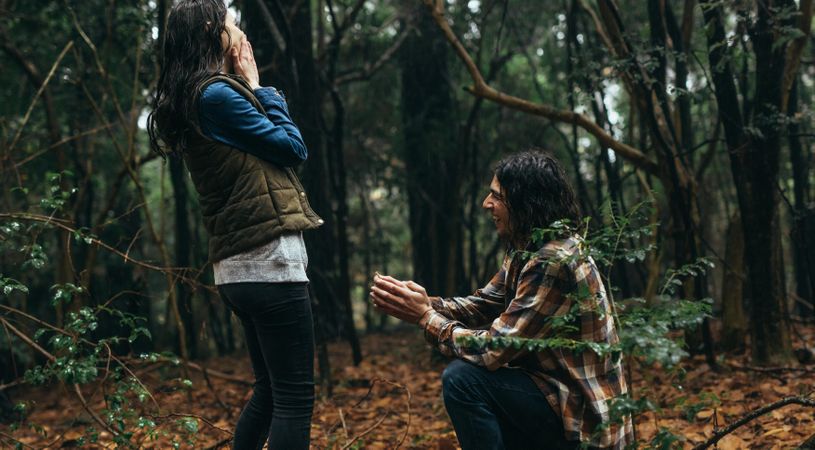 Young man surprising his girlfriend by proposing on their outdoor hike