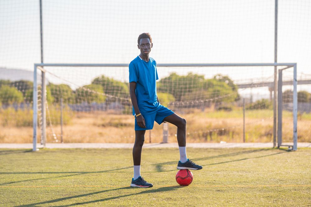 Black football player with ball standing on stadium