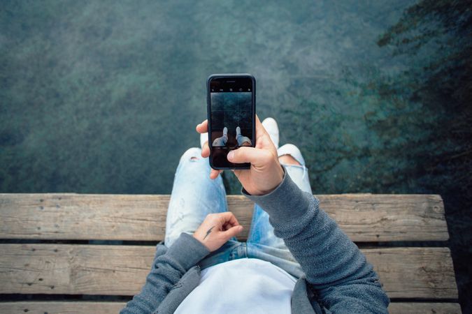 Man sitting on pier taking picture of the water, landscape