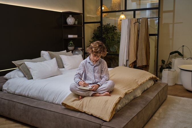 Boy writing in notebook on bed