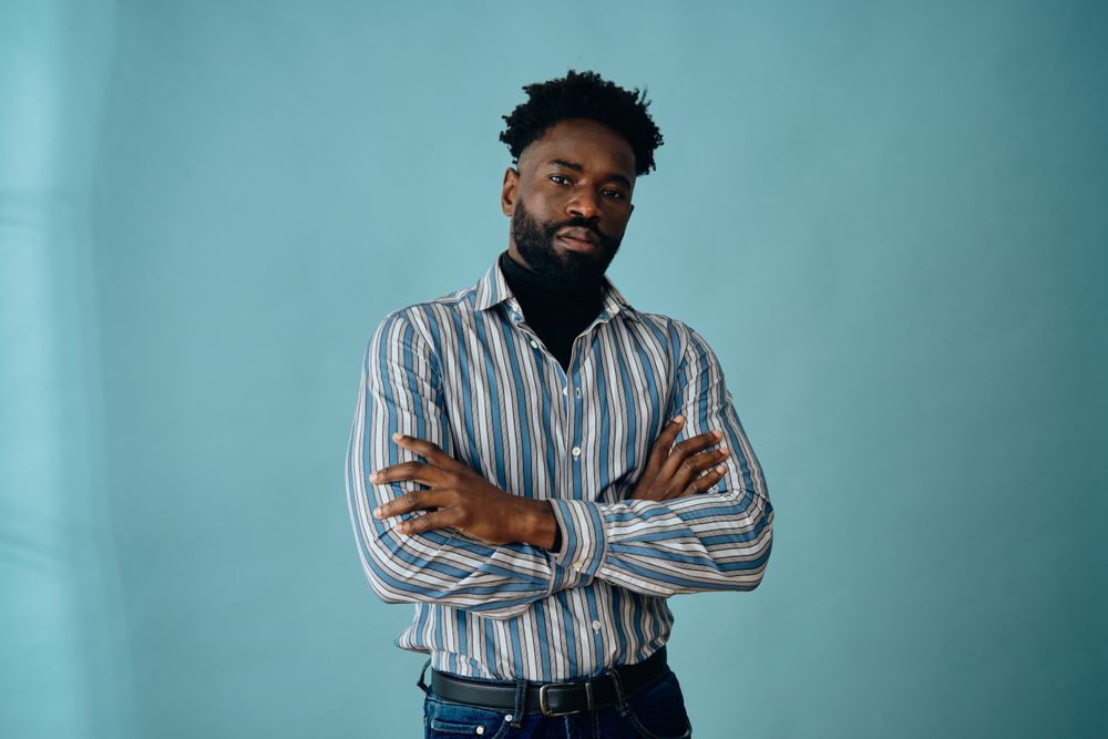 Black man in striped shirt and jeans with his arms crossed