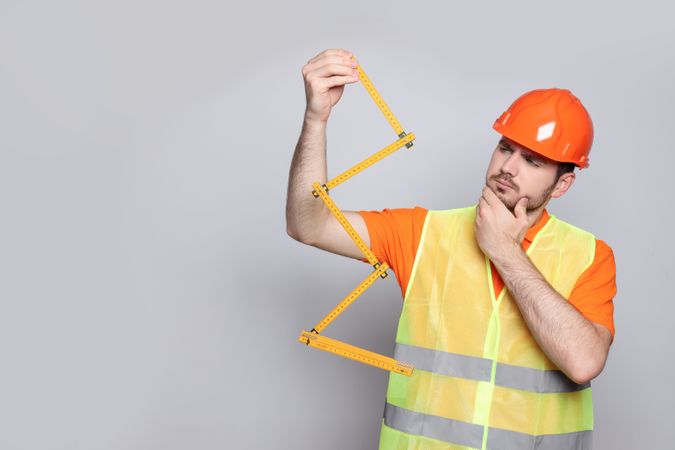 Engineer in helmet with ruler on gray background, space for text