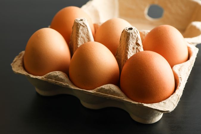 Chicken eggs in carton box on dark background, space for text
