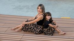 Long-haired mother and daughter sitting on bench back to back