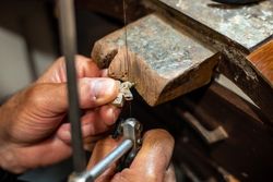 Goldsmith working and creating in his crafting gold jewelry workshop. Jeweler sawing a silver jewel.