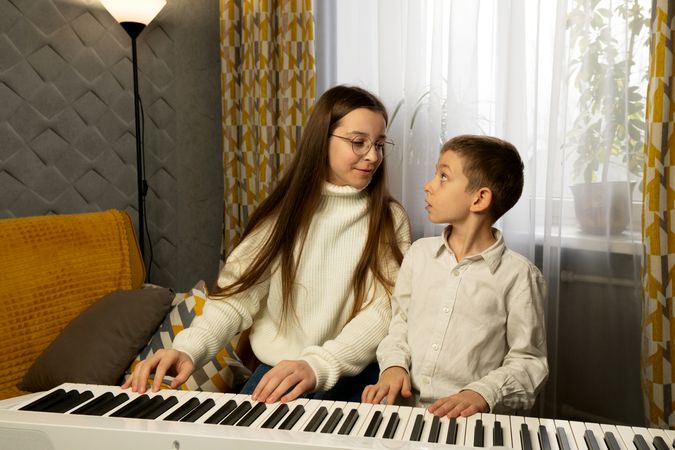 Girl and boy playing piano together while exchanging looks