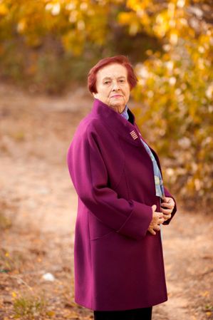 Older woman in purple coat posing near yellow trees