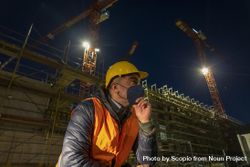 Construction worker with facemask sitting beside a building under construction at night 5kKvj5