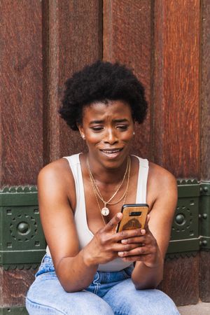 Smiling Black woman using smartphone sitting near building